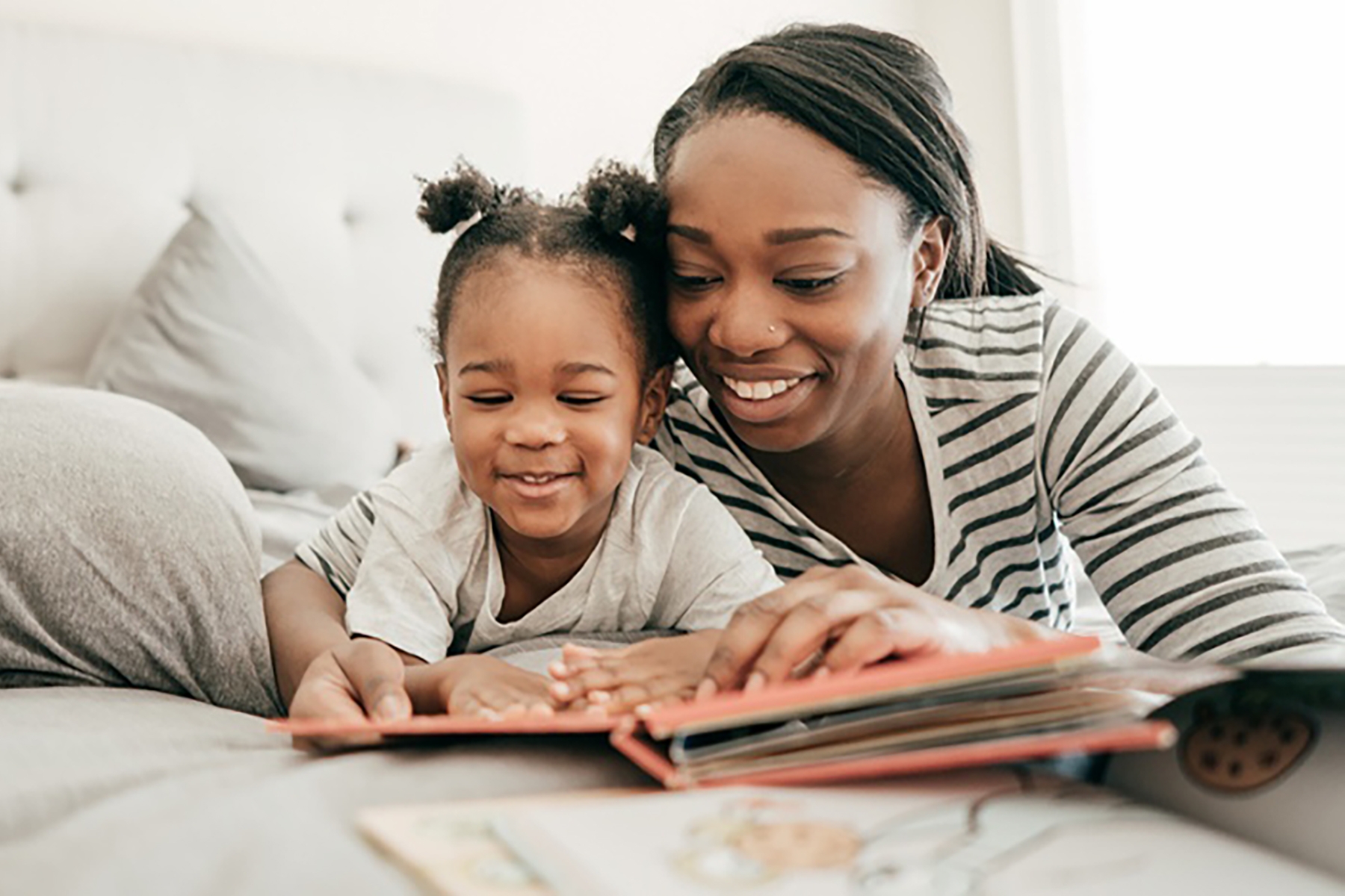 A photo of a mother and young daughter laying on a bed and reading a bedtime story together