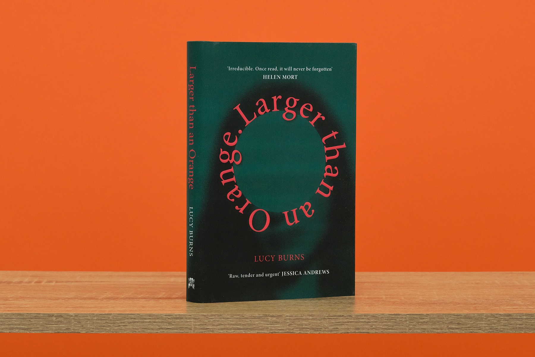 The book Larger Than An Orange stood upright on wooden surface against an orange background