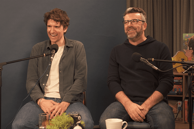Photo of Greg James and Chis Smith smiling in front of their microphones while recording the Penguin podcast